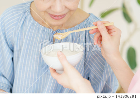 お粥を食べさせてもらう日本人シニア女性と若い日本人看護師の手元 お粥を食べさせてもらう日本人シニア女性と若い日本人看護師の手元 141906291