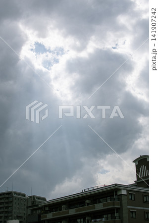 曇り空の切れ間から街並みに向かって優しく降り注ぐ神秘的な光芒の風景 曇り空の切れ間から街並みに向かって優しく降り注ぐ神秘的な光芒の風景 141907242