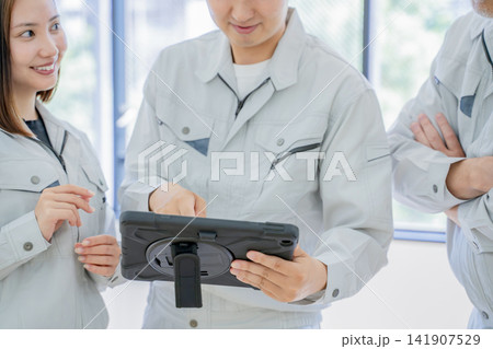 タブレットを見ながら打ち合わせをする作業着の男性と女性 タブレットを見ながら打ち合わせをする作業着の男性と女性 141907529