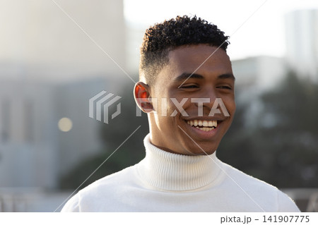 African American man smiling and glancing left on rooftop wearing white turtleneck sweater 141907775