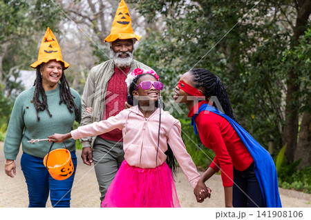 African American family walking along paved garden path wearing pumpkin hats, holding candy bucket African American family walking along paved garden path wearing pumpkin hats, holding candy bucket 141908106