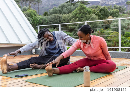 African American couple stretching on rooftop terrace in activewear with mats, phone, water bottle African American couple stretching on rooftop terrace in activewear with mats, phone, water bottle 141908123