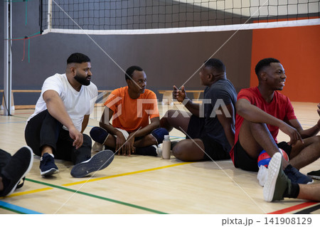 African American men sitting and chatting on hardwood volleyball court near net, wearing knee pads 141908129