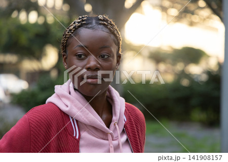 African American woman standing in park wearing pink hoodie and red jacket with braided blonde hair African American woman standing in park wearing pink hoodie and red jacket with braided blonde hair 141908157