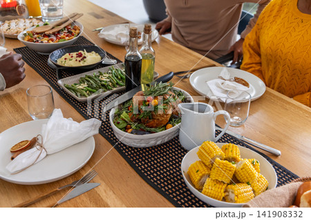 Diverse friends sitting at wooden table eating roast chicken with gravy jug and yellow sweater seen 141908332