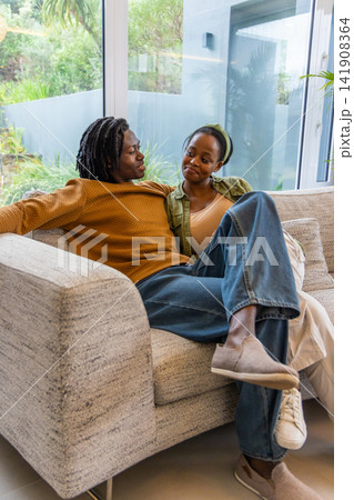 African American couple sitting on gray sofa at home watching garden plants and holding cushions African American couple sitting on gray sofa at home watching garden plants and holding cushions 141908364