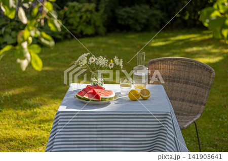 Refreshing Lemon Water and sliced watermelon on Garden Table in Sunny Summer Backyard 141908641