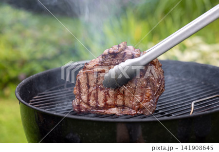 Juicy Beef Steak Grilling on Charcoal Barbecue in Garden 141908645