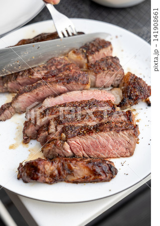 Slicing Freshly Grilled Beef Steak on Plate on Garden Terrace Table Slicing Freshly Grilled Beef Steak on Plate on Garden Terrace Table 141908661
