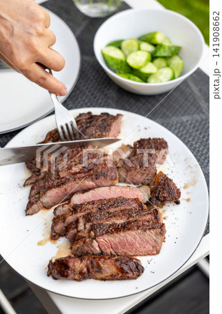 Slicing Freshly Grilled Beef Steak on Plate on Garden Terrace Table Slicing Freshly Grilled Beef Steak on Plate on Garden Terrace Table 141908662