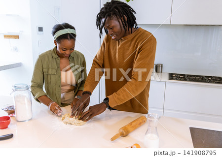 African American couple kneading dough, smiling on white counter in modern kitchen with flour jar 141908795