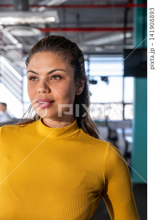 Woman in late twenties standing in modern office wearing mustard yellow turtleneck facing monitors Woman in late twenties standing in modern office wearing mustard yellow turtleneck facing monitors 141908893