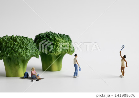 A miniature woman sitting under green broccoli and a couple playing badminton A miniature woman sitting under green broccoli and a couple playing badminton 141909376