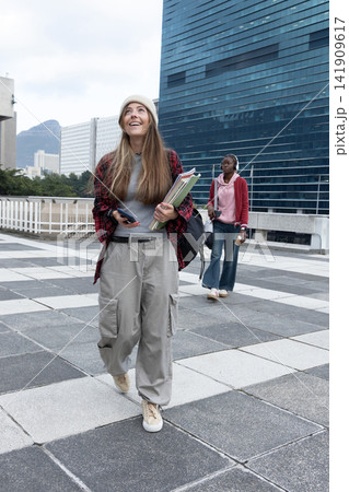 Diverse female students on rooftop wearing beanie and backpack, other wearing headset holding drink 141909617