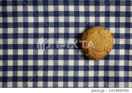 A oatmeal cookie on a blue and white checkered tablecloth A oatmeal cookie on a blue and white checkered tablecloth 141909769