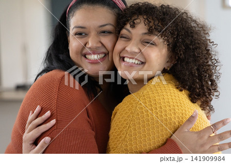 African American female friends hugging, smiling in kitchen wearing rust and mustard sweaters African American female friends hugging, smiling in kitchen wearing rust and mustard sweaters 141909984