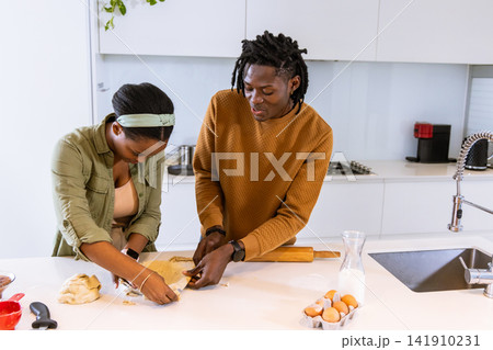 African American couple in casual wear prepping dough with rolling pin and eggs at kitchen island African American couple in casual wear prepping dough with rolling pin and eggs at kitchen island 141910231