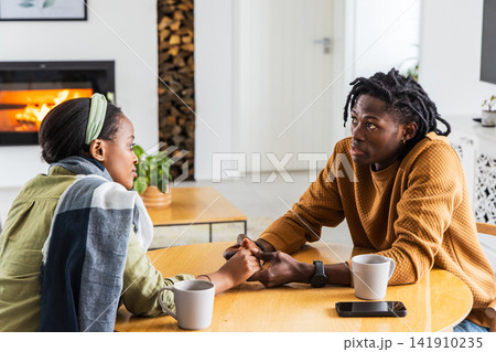 African American couple holding hands talking at round table in living room with phone watch African American couple holding hands talking at round table in living room with phone watch 141910235