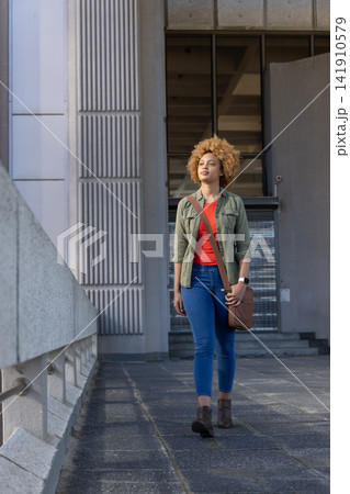 African American woman walking along ribbed path wearing green jacket carrying brown crossbody bag African American woman walking along ribbed path wearing green jacket carrying brown crossbody bag 141910579
