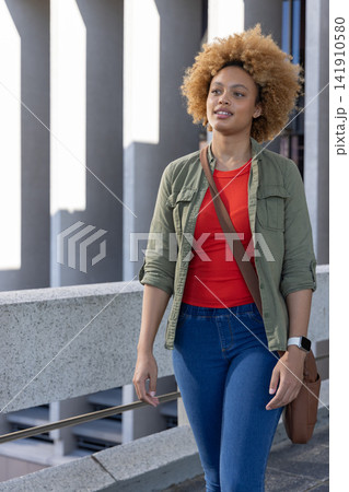 African American woman 20s walking elevated walkway by columns with brown bag checking smartwatch African American woman 20s walking elevated walkway by columns with brown bag checking smartwatch 141910580