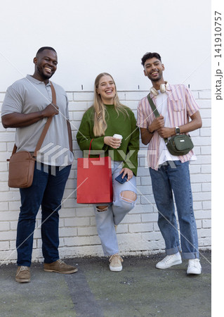 Friends posing against white brick wall holding red bag coffee cup phone wearing green sweater Friends posing against white brick wall holding red bag coffee cup phone wearing green sweater 141910757