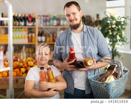Preteen boy with father choosing juices in bottles in supermarket 141911919