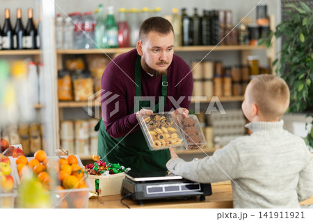 Friendly seller offers cookies to little customer in grocery store Friendly seller offers cookies to little customer in grocery store 141911921