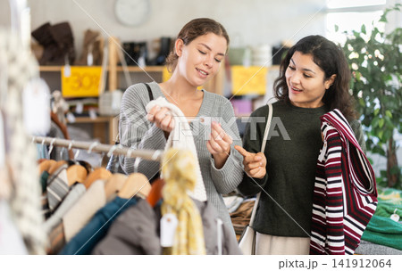 Two women choosing warm sweaters in a store with clothes in the background Two women choosing warm sweaters in a store with clothes in the background 141912064