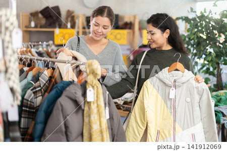 Latin woman with woman companion is busy looking at clothes items, choose winter coat or jacket Latin woman with woman companion is busy looking at clothes items, choose winter coat or jacket 141912069