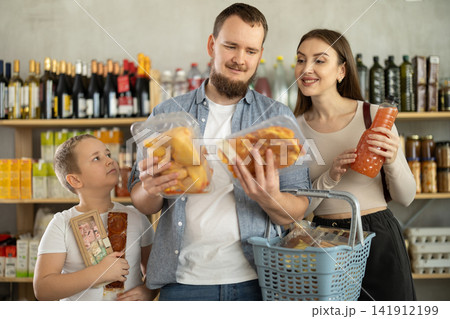 Family with various products in hands continuing shopping in grocery department of supermarket Family with various products in hands continuing shopping in grocery department of supermarket 141912199