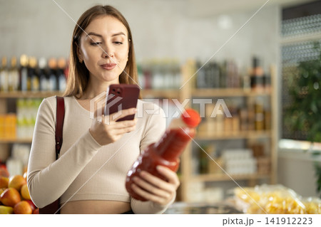 European young woman customer at shop scans QR code on tomato juice bottle using phone camera European young woman customer at shop scans QR code on tomato juice bottle using phone camera 141912223