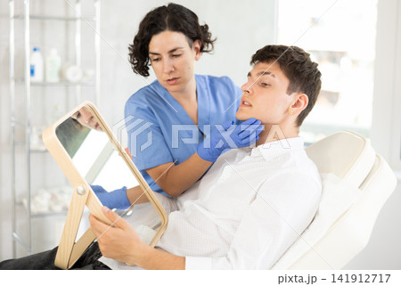 Beautician woman using mirror consulting man in clinic 141912717