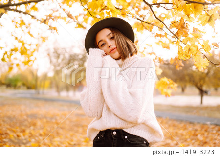 Autumn woman. Young cheerful woman in white sweater and hat walks in the nature park on a sunset. Autumn woman. Young cheerful woman in white sweater and hat walks in the nature park on a sunset. 141913223