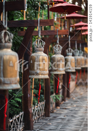 Hanging temple bells with red ropes along wooden walkway in Thailand, Traditional Buddhist metal bells in row with perspective and spiritual atmosphere 141914159