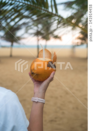 Refreshing coconut drink held by woman on beach at sunset in Sri Lanka 141914458