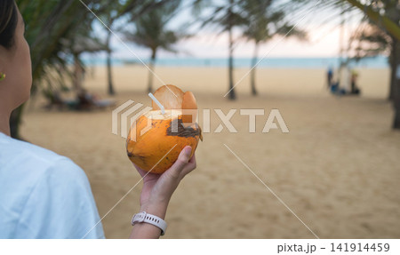 Close-up of woman holding coconut drink at beach during sunset in Sri Lanka 141914459