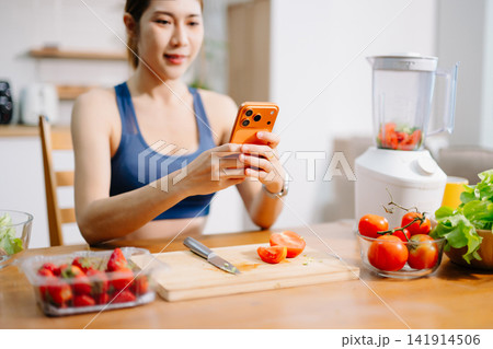 Fitness woman recording healthy smoothie preparation with smartphone in modern kitchen, fresh vegetables and fruit ingredients, healthy lifestyle Fitness woman recording healthy smoothie preparation with smartphone in modern kitchen, fresh vegetables and fruit ingredients, healthy lifestyle 141914506