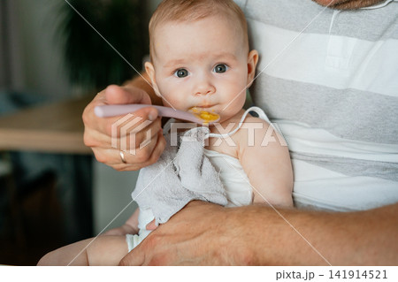 A serene moment of a baby being fed with a plastic spoon, captured in a close-up shot that highlights the calm and nurturing atmosphere of an indoor home setting, with soft white and gray t. A serene moment of a baby being fed with a plastic spoon, captured in a close-up shot that highlights the calm and nurturing atmosphere of an indoor home setting, with soft white and gray t. 141914521