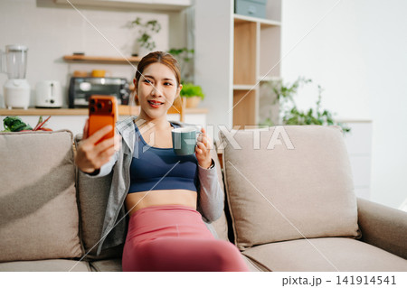 Young woman using smartphone with headphones at home, digital lifestyle, social media, music streaming, mobile app usage in modern living space. Young woman using smartphone with headphones at home, digital lifestyle, social media, music streaming, mobile app usage in modern living space. 141914541