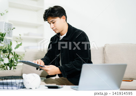 Young man using a tablet for budgeting and financial planning at home. Savings, fintech, money management, investment goals and digital finance concept. 141914595