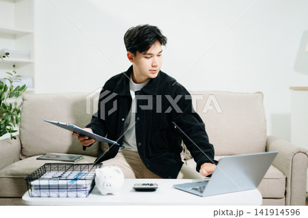 Young man using a tablet for budgeting and financial planning at home. Savings, fintech, money management, investment goals and digital finance concept. Young man using a tablet for budgeting and financial planning at home. Savings, fintech, money management, investment goals and digital finance concept. 141914596