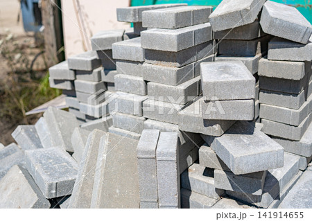 Stacked concrete pavers stacking, in construction site, with concrete pavers, construction materials, from a close-up perspective, with gray, green accents, and industrial work-in-progress mood. 141914655