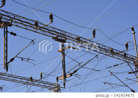 Railway catenary steel gantry with intricate overhead lines against a blue sky Railway catenary steel gantry with intricate overhead lines against a blue sky 141914675