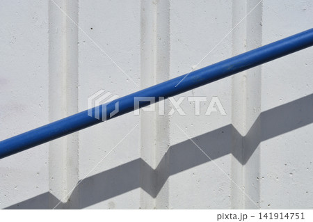 Blue metal handrail with geometric shadow on a white concrete wall Blue metal handrail with geometric shadow on a white concrete wall 141914751