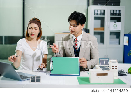 Business professionals using solar and wind models to plan sustainable green energy and ESG initiatives in a modern corporate office. 141914820