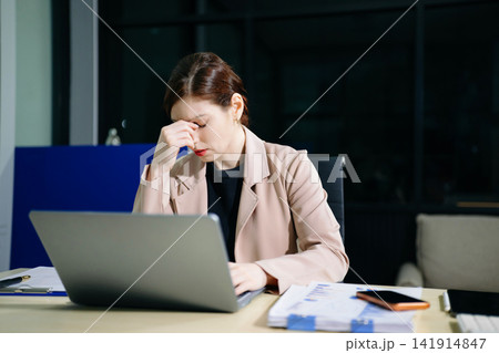Asian woman feeling migraine head strain.Overworked businesswoman financier while working on laptop and tablet at office. 141914847