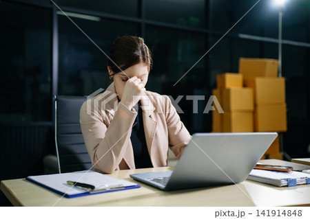 Asian woman feeling migraine head strain.Overworked businesswoman financier while working on laptop and tablet at office. 141914848