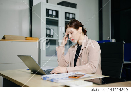 Asian woman feeling migraine head strain.Overworked businesswoman financier while working on laptop and tablet at office. 141914849