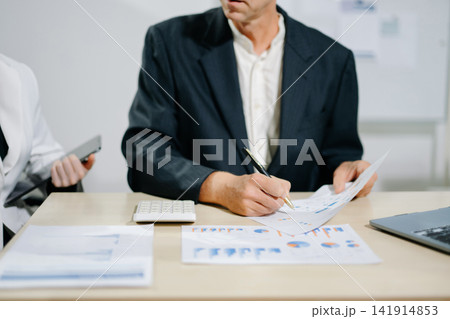 Business documents on office table with smart phone and calculator digital tablet and graph business with social network diagram and two colleagues discussing data working in the office 141914853