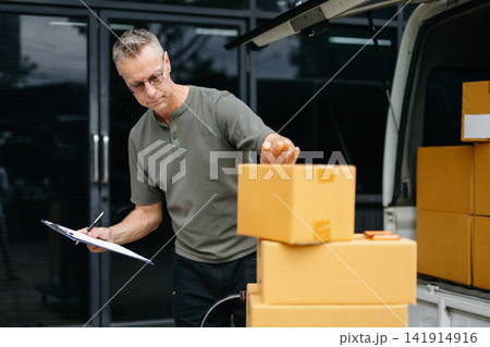 Warehouse worker inspecting parcels with clipboard before loading delivery van. Logistics, inventory, ecommerce shipping, supply chain, fulfillment a Warehouse worker inspecting parcels with clipboard before loading delivery van. Logistics, inventory, ecommerce shipping, supply chain, fulfillment a 141914916